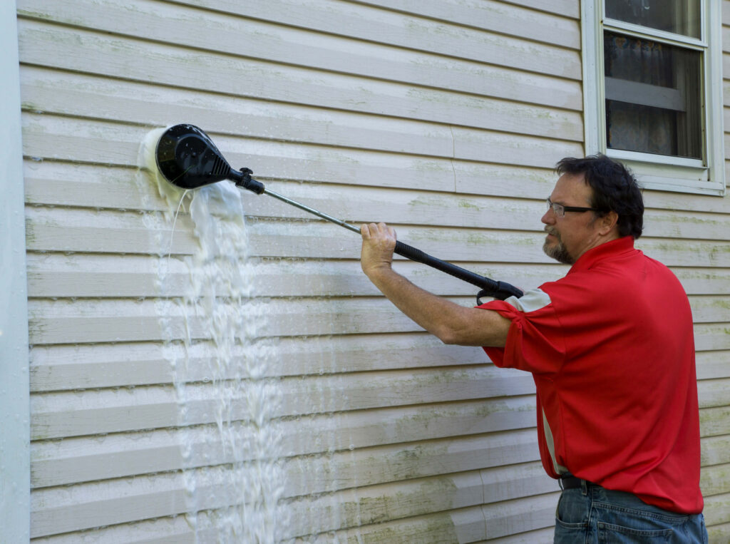 Using a high pressure brush to clean algae and mold off vinyl siding.