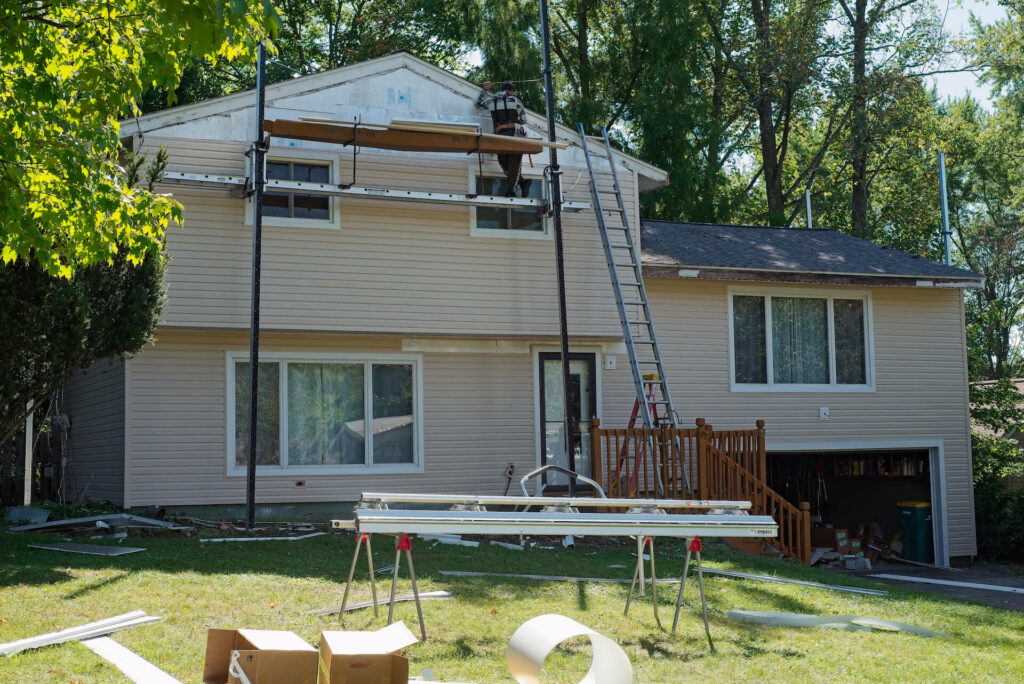 A home siding replacement project nears completion with new siding installed on all but the very top of a split-level suburban house.
